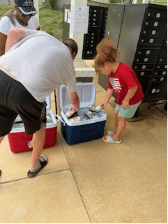 Man and little girl grabbing drinks from an ice cooler.